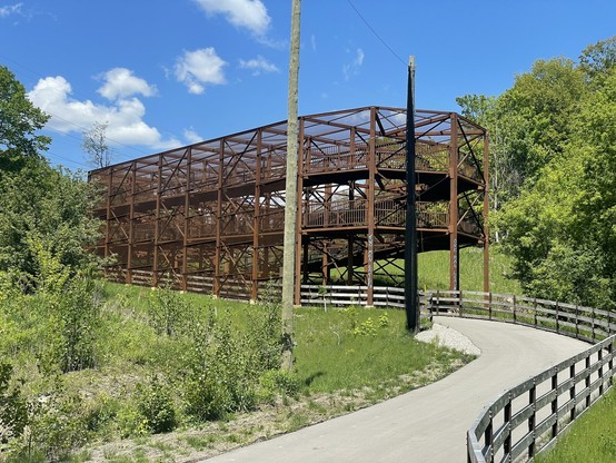 A bike path leads to a large metal switchback structure, where you can ride a ramp up two levels then cross a train track.  Surrounding it are leafy trees.
