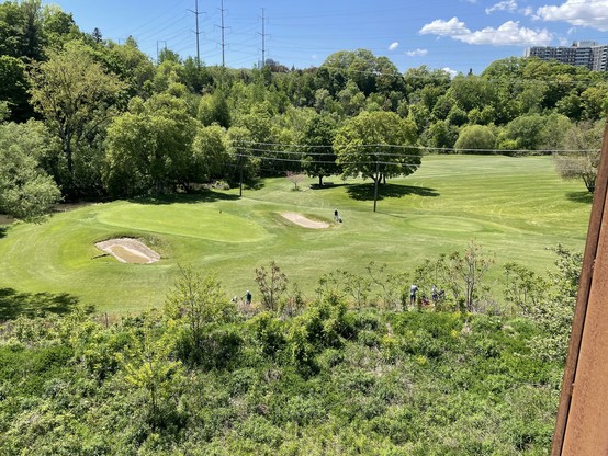A view of the Don Valley Golf Club from the switchback structure, showing two sand traps, a well-mowed green, and a small group of golfers playing.