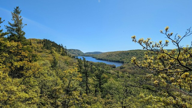 A wide vista, looking back towards Lake of the Clouds nestled between low hills (ancient mountains) with foreground trees framing the picture.