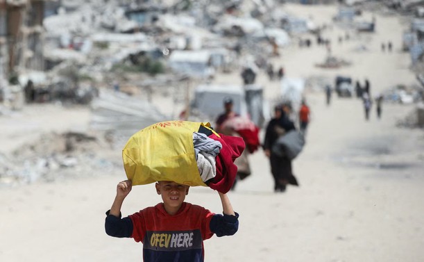 A boy carrying a bag with his clothes on his head.