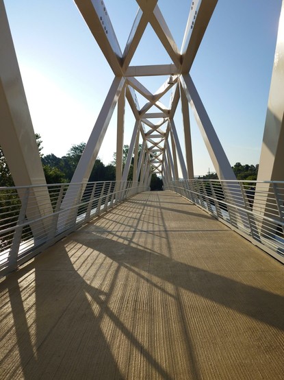 A modern pedestrian bridge with geometrical shapes.
Trees at the bottom.
Sunny weather