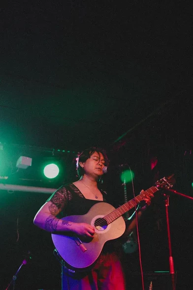 Dwi Riana live on stage playing an acoustic guitar.