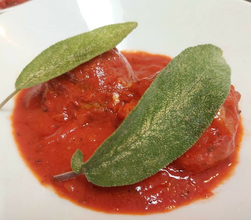 A bowl with two big meatballs, drowned in tomato sauce and garnished with basil leaves