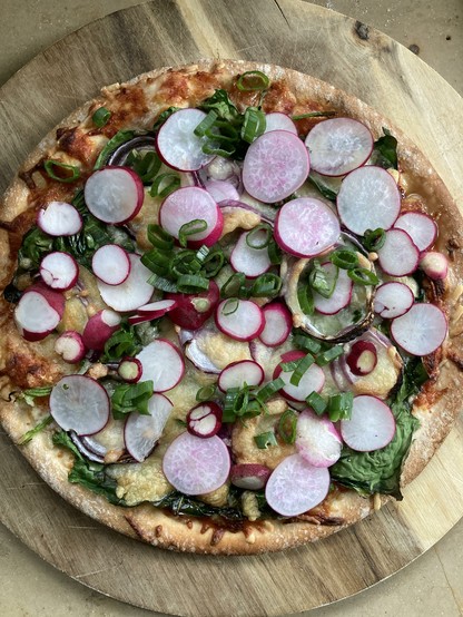Eine runde Spinatpizza mit reichlich aufgeschnitten Radieschen belegt.
