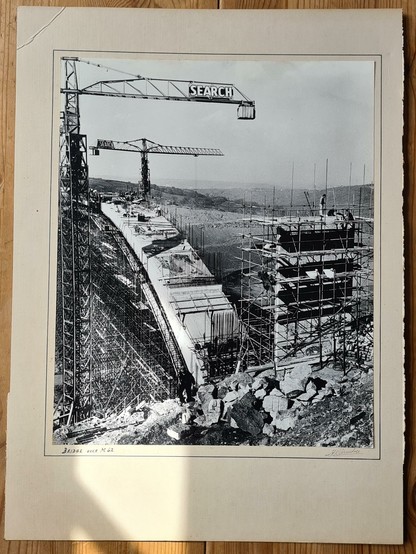 A photo of a black and white photo, in an off white mount. The framed picture is of a massive arched bridge under construction, its concrete arch held up with an unbelievable amount of scaffolding. There are various cranes visible too. It looks like an awful lot of work to make the bridge. The image is captioned "Bridge over M62" and is from the late 1960s.