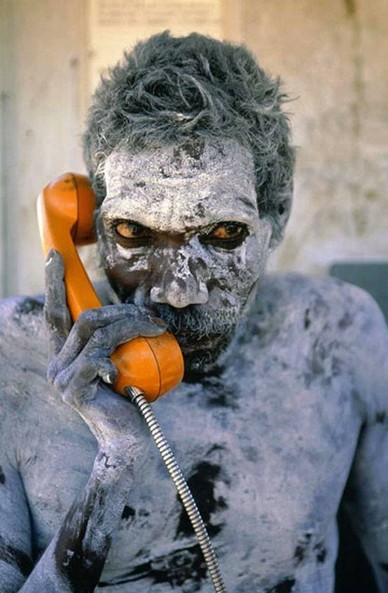 In the photo you can see an Aboriginal man in ritual make up, holding an orange phone.