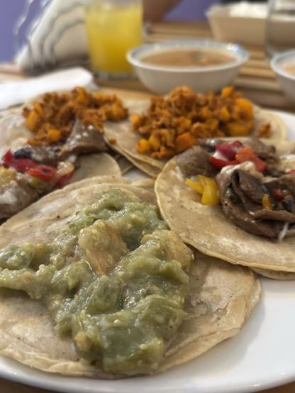 Fotografía de cinco tacos dos de chorizo de soya con papas, dos de asada de seitán con pimiento Morton rojo y amarillo, queso vegetal, uno de chicharrón de trigo en salsa verde.