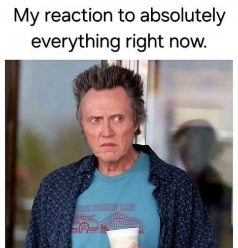 Dressed casually, Christopher Walken scowling while stepping out of a coffee shop with a cup of coffee... that he needs to drink pronto