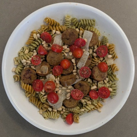 Pesto noodles with fried onion, sausage, sliced cherry tomato, and pine nuts with olive oil and black pepper on top