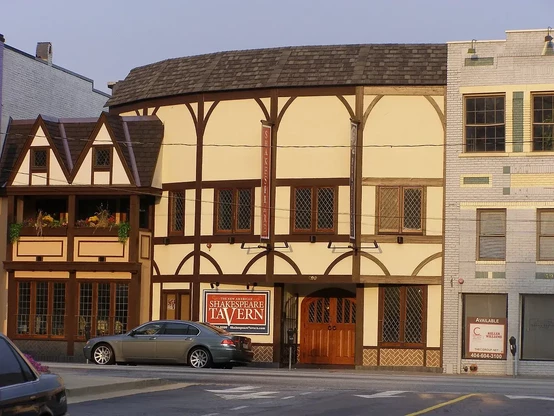 The image features a building designed in a Tudor-style architecture, characterized by its half-timbering and decorative features. It displays signs indicating that it is the "Shakespeare Tavern," suggesting that the establishment may be a theater or restaurant with a focus on Shakespearean plays. The structure is located on a street, with a car parked in front. The surrounding buildings have a more modern design compared to the traditional style of the Shakespeare Tavern.

Image Credits: Wikimedia / Greg Hanthorn, Jr (Hanthorn98 (Uploads)) / Public domain