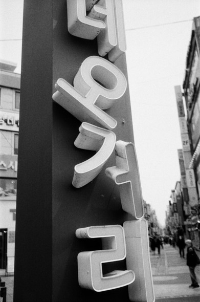 세로쓰기로 '로데오거리'라 쓰인 간판. '오'자와 '거'자가 삐뚤빼뚤 어긋나있다.