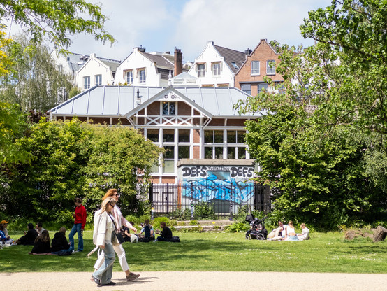 People relaxing on the grass near a building with graffiti in Vondelpark, Amsterdam.
