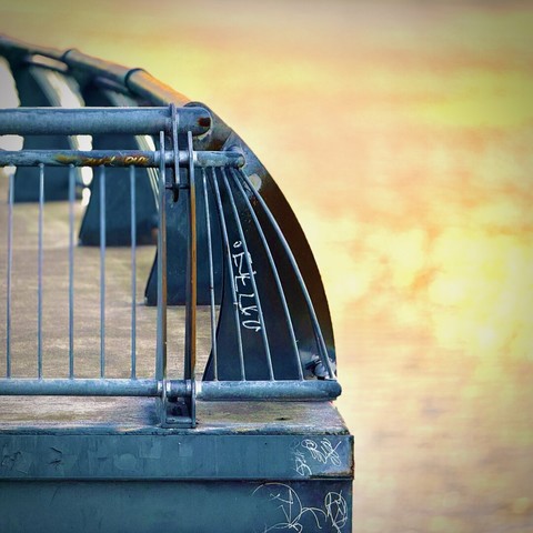 The shaded corner of a concrete viewing platform with metal, ninety-degree railing basks in the reflected rising sunlight of the Willamette River.
