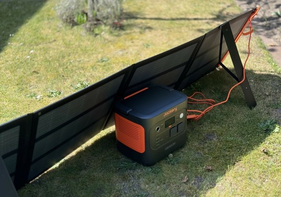 Jackery Explorer 2000 v2 Powerstation samt angeschlossenem SolarSaga 200W-Solarmodul steht auf einer Rasenfläche in der Sonne.