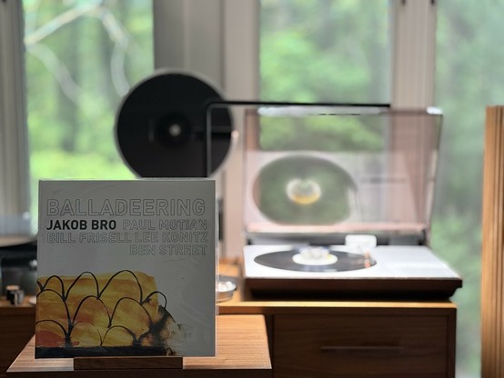 Jakob Bro - Balladeering LP cover.

Mostly white, top half with the title and most names in black outline, except for Bro, whose name is all black.

Below, what look like eggs and a bird, maybe.

The black LP plays on a vintage, restored Bang & Olufsen Beogram 4000 linear-tracking turntable to the right.
