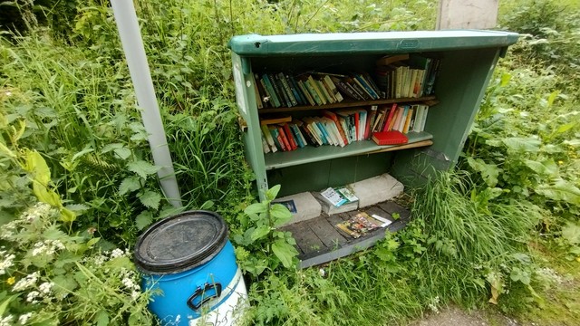 A bookcase found on the towpath. of the Bridgewater Canal. Beside it is a blue bin with a notice saying "poo bags only" (or something to that effect)