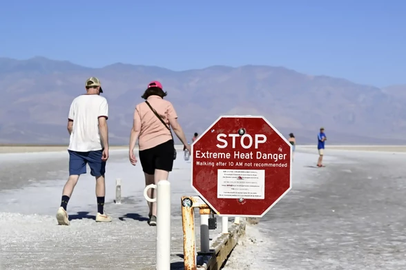 Tourists in Death Valley NP. The warning sign reads:
STOP
Extreme Heat Warning
Walking after 10am is not recommended.