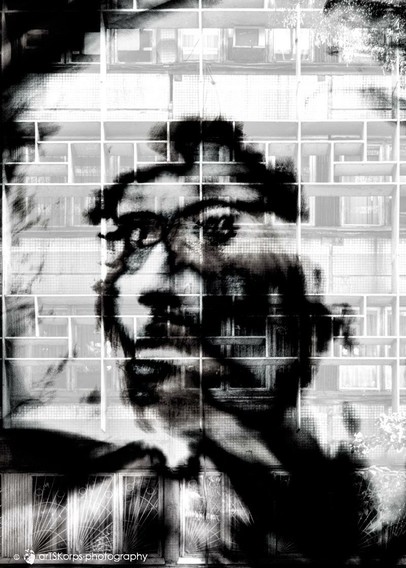Black and white photo, portrait format, multiple exposure, self-portrait (headshot, motion blur, high-contrast). Against a light, textured background (the facade of an apartment block consisting of numerous windows), the silhouette of a face looking sideways, barely recognizable as such. The eyes appear to be sadly directed into the distance. The overall impression is one of hopelessness, despair, but also of holding oneself captive with one's own feelings.