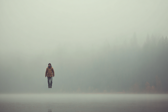 Person hovering above a fog-covered body of water with a misty forest in the background.