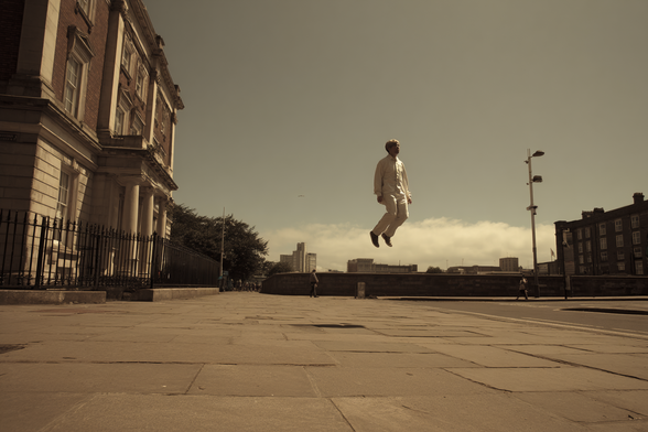 Person floating in mid-air on a paved urban sidewalk beside a large building.
