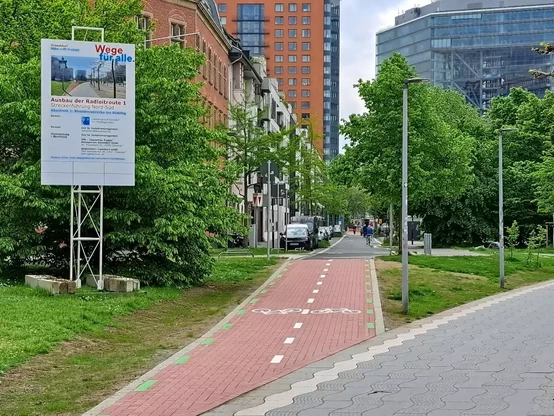 Der neue Radweg am Landtag/Stadttor, der von der Rheinuferpromenade zur Moselstraße führt. Links im Bild ein großes Schild der Stadt, das den Ausbau der Radleitroute 1 ankündigt. (Foto: Klaus Kurtz)