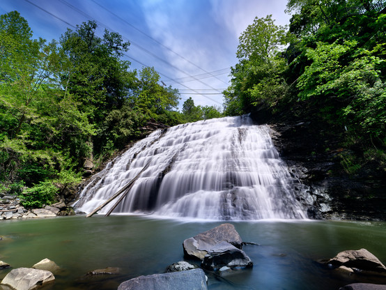 large waterfall with flowing water from the longer exposure with blue cloudy skies, and trees and greenery on the sides of the waterfall