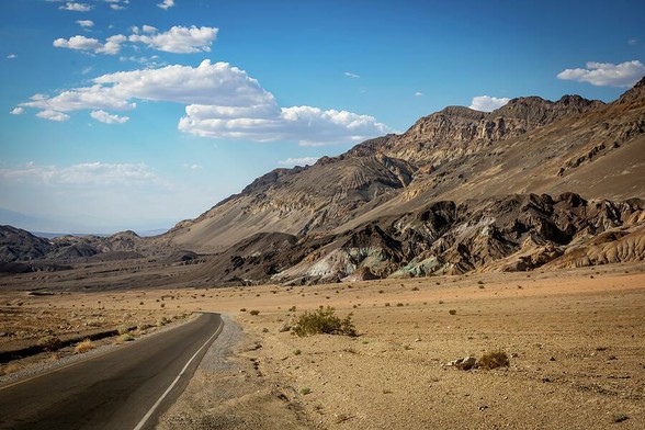 A winding road through the vast, arid landscape of Death Valley National Park, California, with rugged mountains under a clear blue sky.
