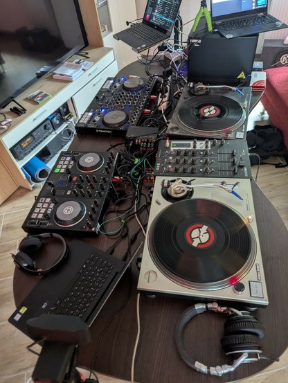 A crazy DJ Table setup with 2 controllers, turntables and a mixer, lots of crazy cabling and complete madness.