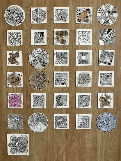 31 different Zentangle tiles laid out on a wooden floor, showing what I have drawn this month