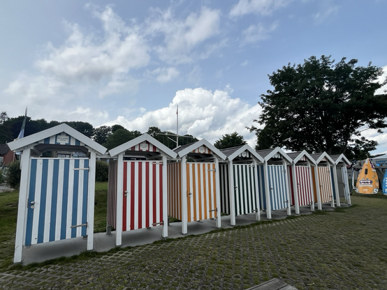 Acht bunt, gestreifte Umkleidekabinen an der Kieler Förde. Blauer Himmel mit einigen Wolken