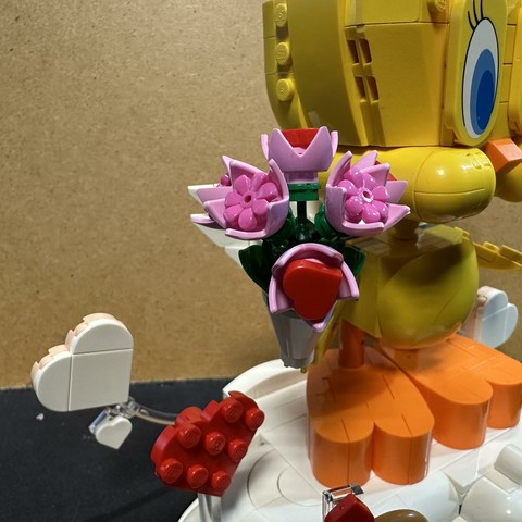 A Lego model of tweety the bird from Looney Tunes, holding a flower bouquet while standing on a cloud with hearts. Cupido’s bow and arrow are also included for some reason.