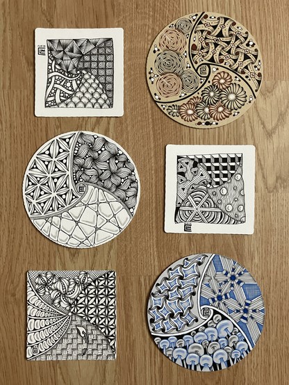 Three square tiles, each containing four patterns, and three round Zendala tiles, each containing three patterns, laid out on a wooden floor.