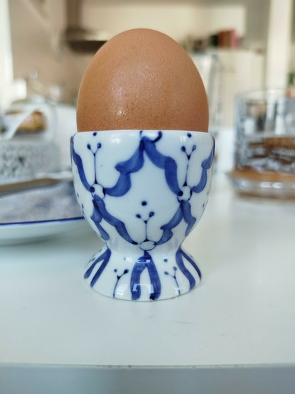 Ein braunes ei in einem blau weißen Porzellan Eierbecher. Das Dekor sieht aus Versehen auf der einen Seite so aus wie ein Gesicht