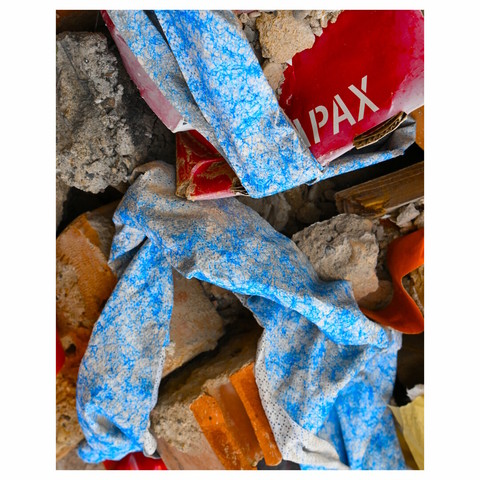 A closeup of some debris in a trash container, with cardboard pieces with blue sprinkles and a red piece of a cardboard packages with a partially hidden text, only the letters "PAX" are visible.