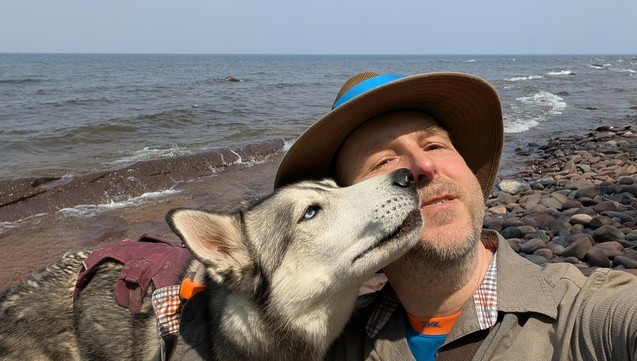 Dale and Tonttu pose for another selfie, this time with wide Lake Superior to their back, Tonttu is poking his muzzle up and into Dale's face, while he leands back and squints against both the sunlight and Tonttu's invasion of his personal space.