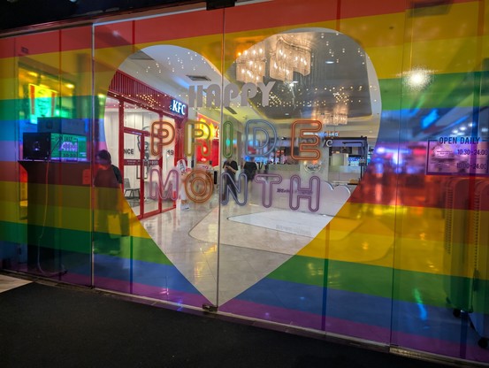Happy Pride Month written within a heart shaped sticker across two sliding doors. On each side of door are colorful striped colors representative of Pride Month. Captured with Google Pixel in Bangkok Thailand