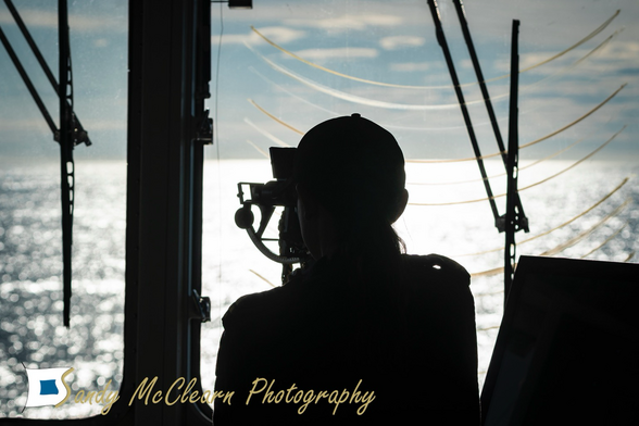 Sailor on a ship’s bridge using a sextant in silhouette.