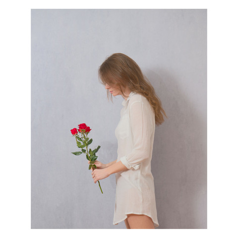 Artistic portrait of a woman in a white short holding a red rose