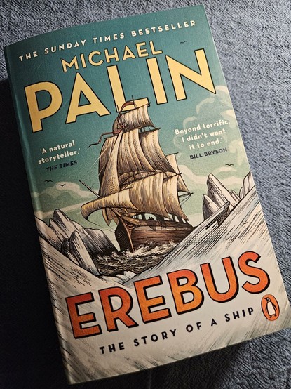 Paperback auf blauem Tischtuch. Das Cover zeigt ein Segelschiff bei der Einfahrt in eine von Packeis umgebene Bucht.