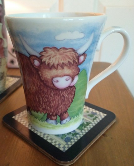 Mug of tea on a bedside cabinet with a Highland cow in a field.