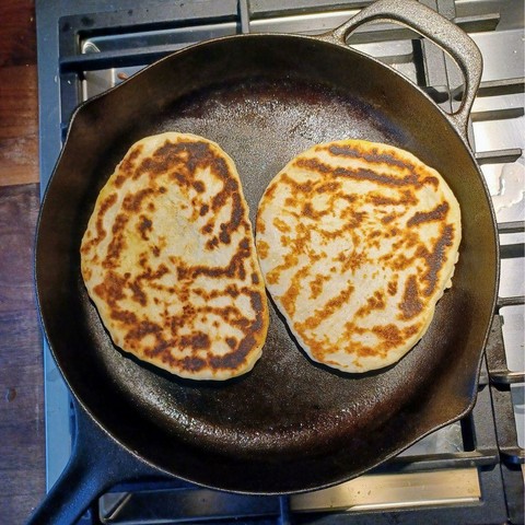 A view from above of 2 naan baking in a cast iron skillet.
