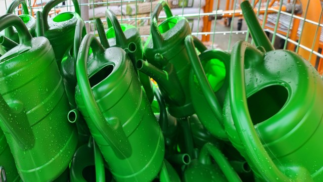 Drahtgitterbox voll grüner Plastik-giesskannen vor dem Obiladen