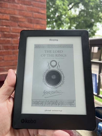 An e-reader displaying "The Lord of the Rings" cover, illustrated by the author, with a reading progress of 37% and an estimated 20 hours left. The background shows greenery and a brick wall.