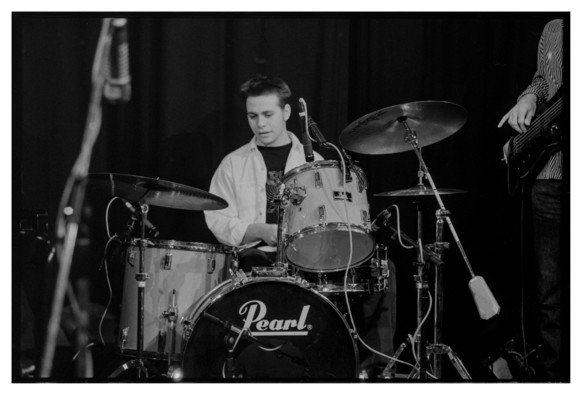 Black and white photograph of a drummer behind his drum kit.