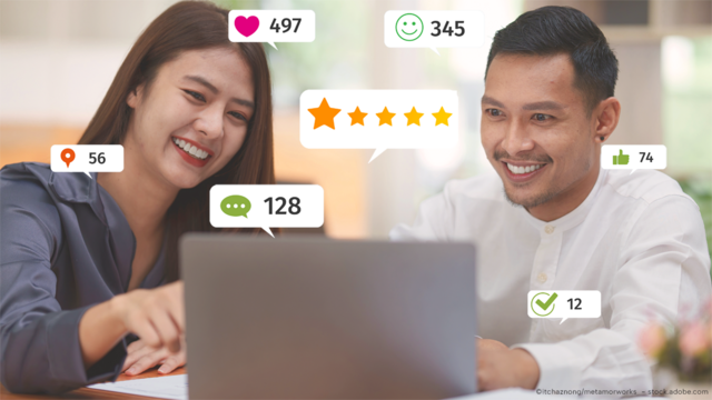 A woman and a man are sitting in front of a laptop. They are both smiling. In the picture, there are emojis, dislikes, green smileys, hearts, and 5-star ratings floating around.