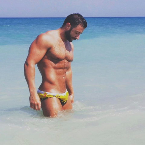 A muscular white man wearing yellow speedos is coming out of the sea
