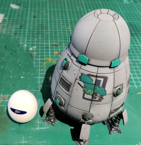 A grey Overlord-C DropShip miniature with jade highlights and some gentle battle damage on its surface. The miniature is standing on a well-worn green cutting mat, and it has a nougat-filled Mignon egg standing next to it for scale and silliness.