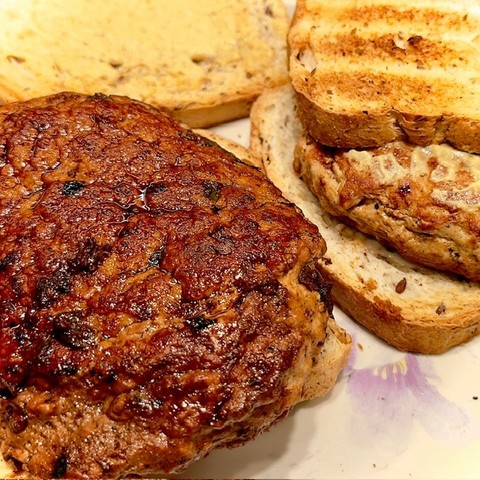 Two thick turkey hamburgers are shown sitting on toasted bread upon which mustard has been spread. The burger on the left is covered with pan deglazing that makes it look caramelized and especially delicious. The burger on the right does not show any deglazing, but looks tasty nonetheless. Both burgers were fabulous and fluffy.