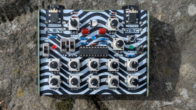 Top-down photo of Levitation Oscillator. 13 pots, a few buttons and switches, twin-peaks aesthetics, ATMEL microcontroller in the center.