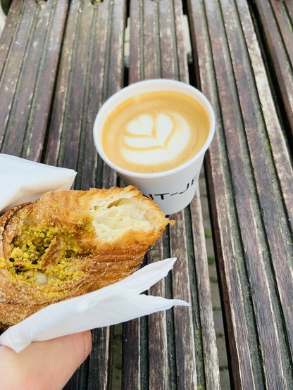 A picture of a pistachio cruffin and a cappuccino with latte art.